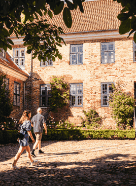 Et ungt par ses på opdagelse i en hyggelig solbelyst baggård i Viborg Domkirkekvarter. foto: Visit Aarhus