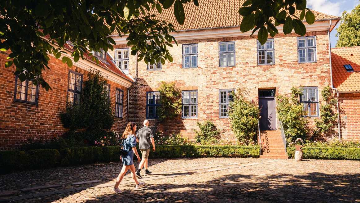 Et ungt par ses på opdagelse i en hyggelig solbelyst baggård i Viborg Domkirkekvarter. foto: Visit Aarhus
